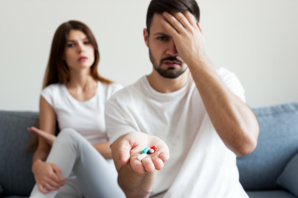 frustrated man holding a handful of pills, looking at his partner with disappointment